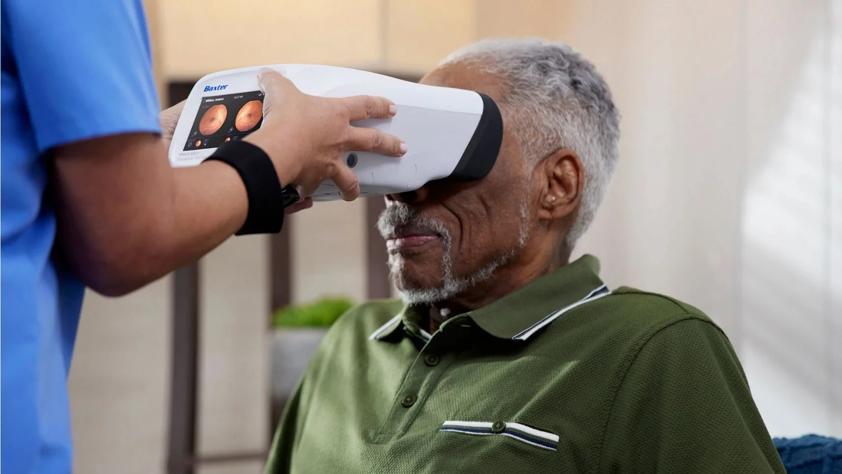 Healthcare worker holds the RetinaVue 700 to the face of an elderly man. The screen of the device shows retinal imaging